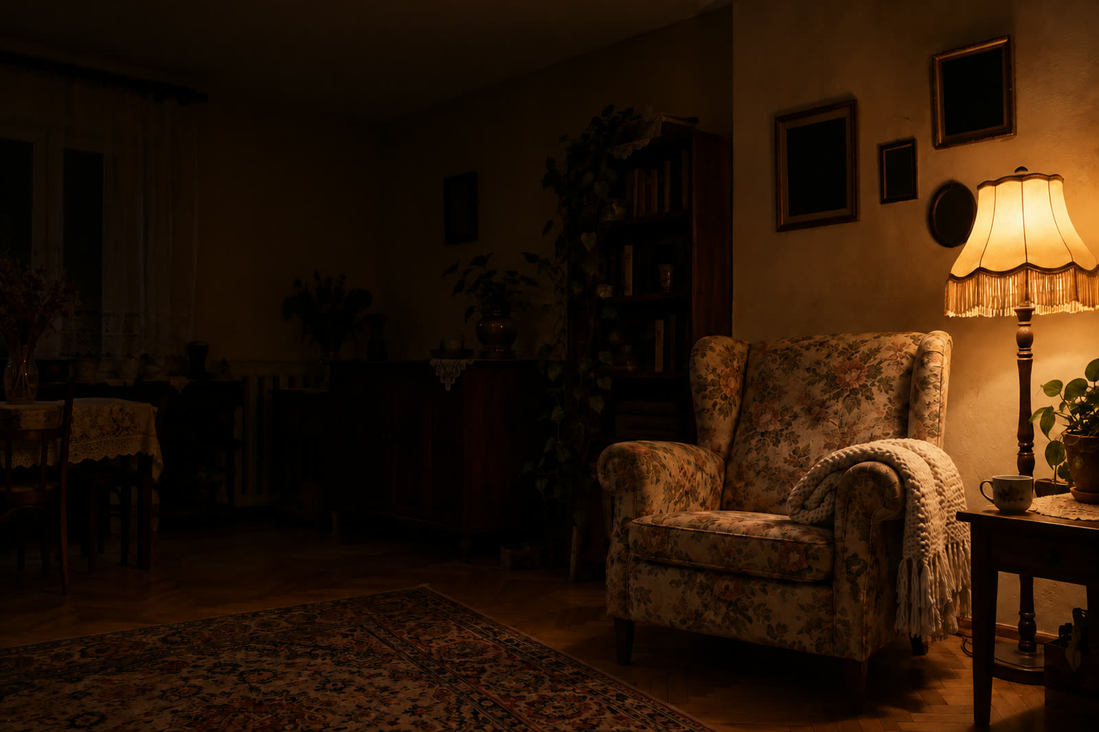 An empty floral armchair beside a lit lamp in a dark room